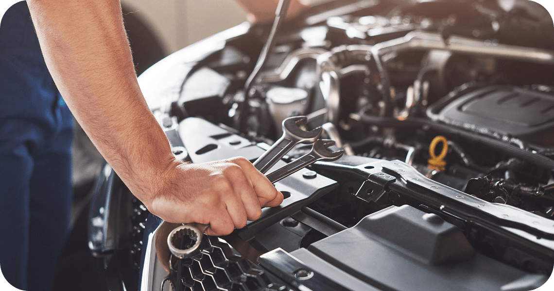 A technician holding wrenches over an open car engine.
