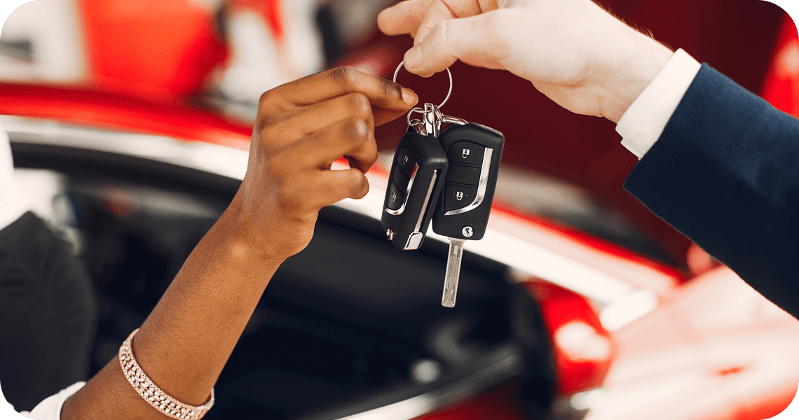 Car keys being handed over beside a red vehicle.