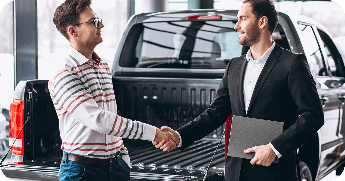 Two people shaking hands beside a pickup truck.
