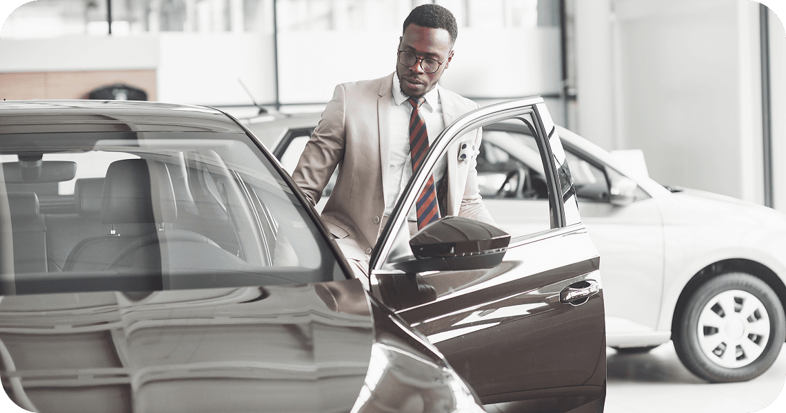 A man in a suit opening the door of a car in a showroom.