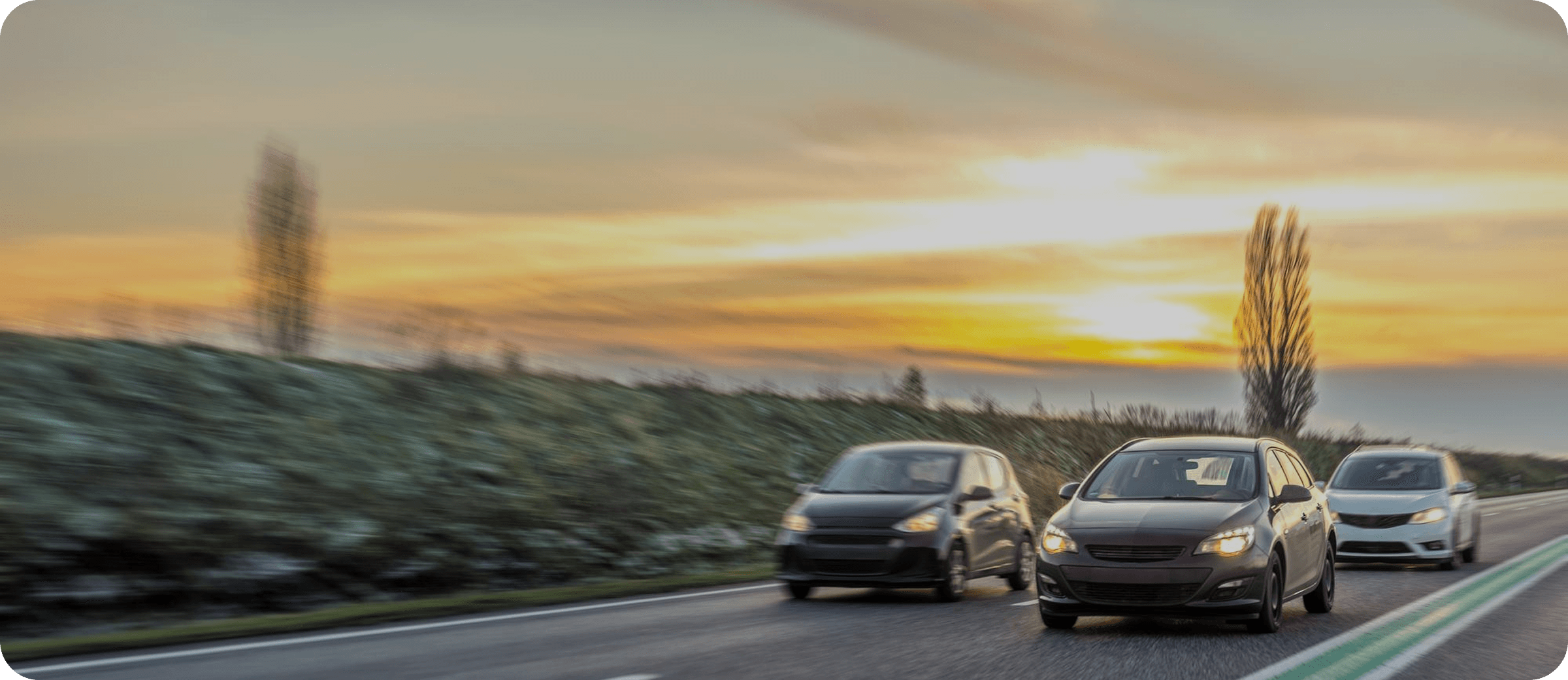 Three cars driving on a highway at sunset.