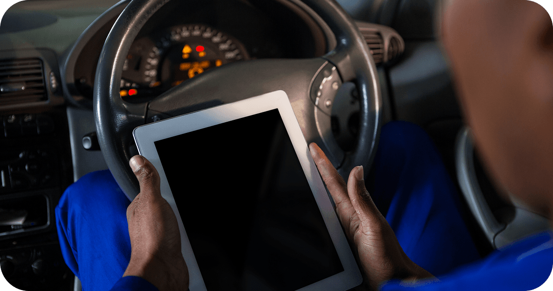 A driver holding a tablet at the steering wheel.
